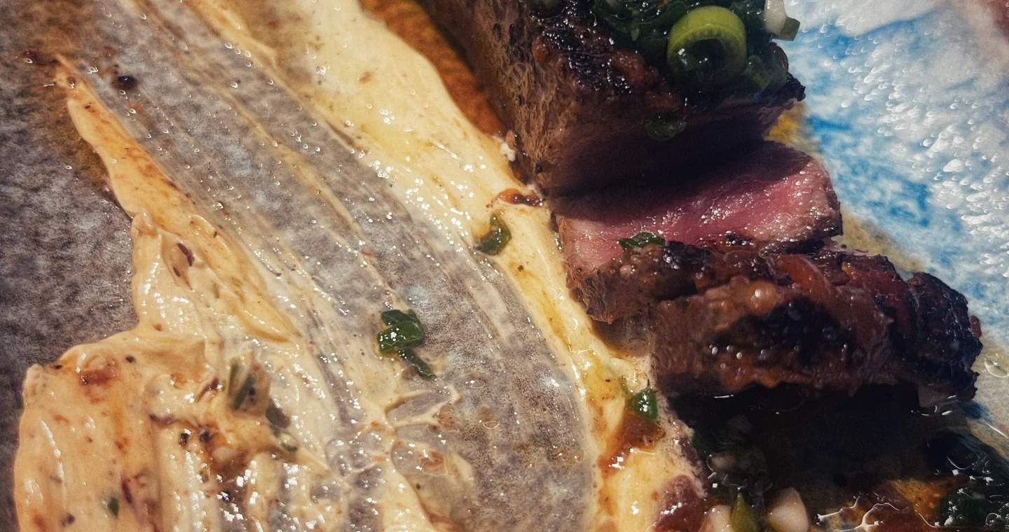 A close view of a fillet of fish in a pale sauce beside slices of seared steak