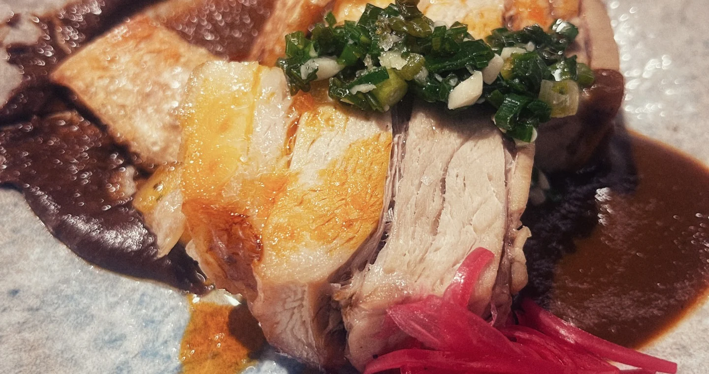 Sliced chicken with a green herb topping on dark mole sauce, with pink pickled onion
