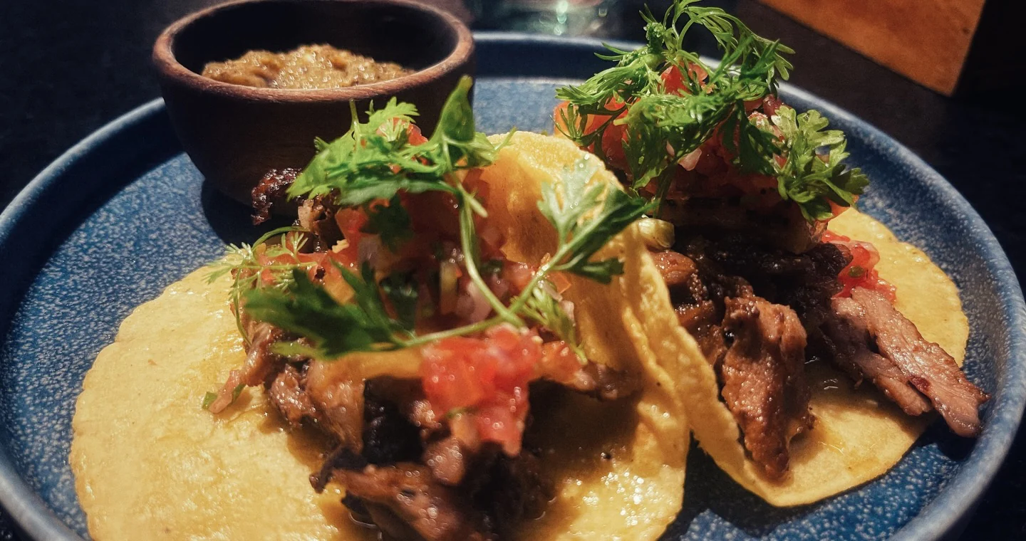 Two tacos piled with meat, tomato and herbs on a blue plate